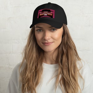 May include: Black baseball cap with a front panel featuring a pixelated image of a red car. The car image is set against a pink background. The cap has a curved brim and an adjustable strap.