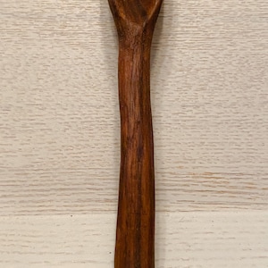 May include: A wooden spoon with a dark brown finish. The spoon has a long, curved handle and a rounded bowl.