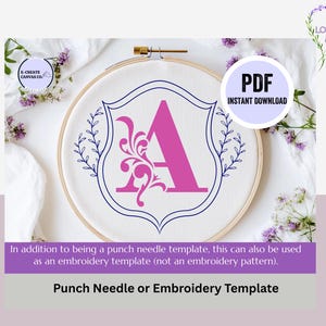 May include: A digital download PDF template for punch needle or embroidery featuring a pink letter A with a decorative flourish inside a blue shield with leafy branches on either side. The template is displayed on a white embroidery hoop.