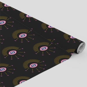 May include: Black wrapping paper with a repeating pattern of gold and pink evil eyes. The eyes have blue pupils and are surrounded by gold rays.