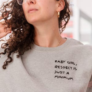 May include: A gray sweatshirt with the text "Baby girl, respect is just a minimum" written in black marker.