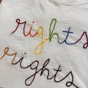 May include: White t-shirt with the word "rights" embroidered in rainbow colours.
