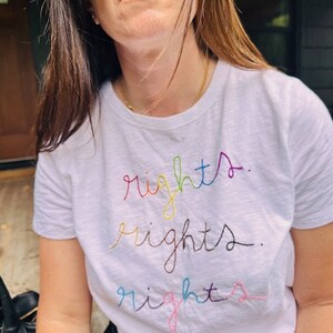 May include: A white t-shirt with the word "rights" embroidered in rainbow colours.