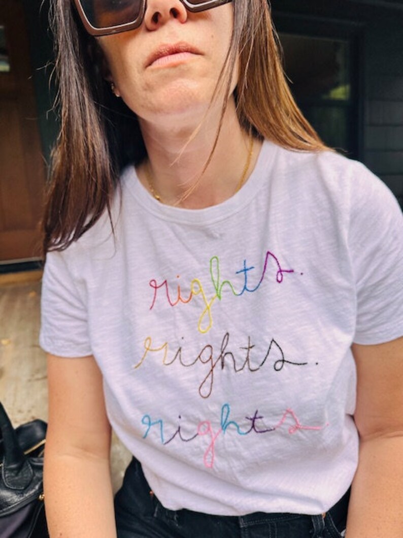 May include: A white t-shirt with the word "rights" embroidered in rainbow colours.