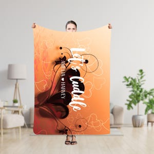 Puede incluir: Una manta suave de color naranja y marrón con un diseño floral blanco y el texto "Let's cuddle" en blanco. Los nombres "Amelia ♥ Harvey" están escritos en negro debajo del texto.