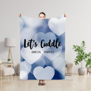 Puede incluir: Una manta azul y blanca con un patrón de corazones y el texto "Let's Cuddle Amelia ♥ Harvey".