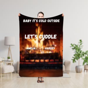 Puede incluir: Una manta de franela negra con una imagen de chimenea y el texto "Baby it's cold outside Let's cuddle Amelia Harvey".
