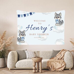May include: A light blue baby shower banner with the text "Welcome to Henry's Baby Shower 31 October, 2025". The banner features illustrations of gray wolf cubs with blue bows and clouds. Blue pennant banner at the top.