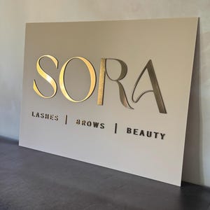 May include: A handmade wooden sign with the word "Welcome" in a whimsical font. The sign is painted white with a distressed finish, and features a floral design in pinks and greens. It measures approximately 30 cm wide.