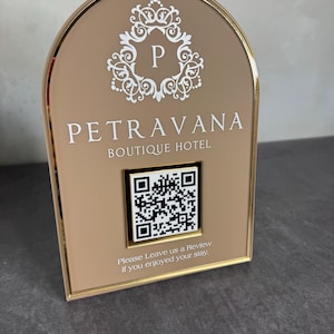 May include: A gold-framed sign with a beige background displays the text "PETRAVANA BOUTIQUE HOTEL" and a QR code. The sign also includes the text "Please Leave us a Review if you enjoyed your stay."