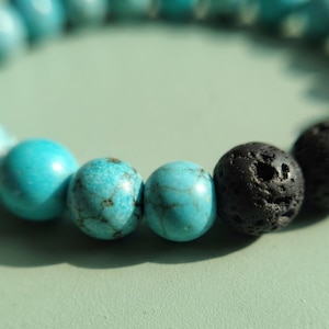 Peut inclure: Un bracelet de perles composé d'une alternance de perles turquoise lisses et rondes avec des veines sombres et de perles de pierre de lave noire mates, poreuses et texturées. Les perles sont assemblées en cercle sur un cordon élastique.