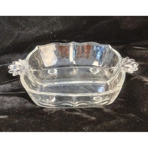 May include: A clear, divided glass serving dish with a scalloped rim and decorative handles. The dish is rectangular with three compartments, suitable for serving snacks or appetizers. The handles have a floral design.
