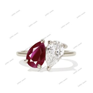 May include: A silver ring featuring two pear-shaped gemstones. One is a deep red ruby, and the other is a clear, sparkling diamond. The gemstones are set side-by-side, creating a unique and elegant design. The ring is set against a white background.