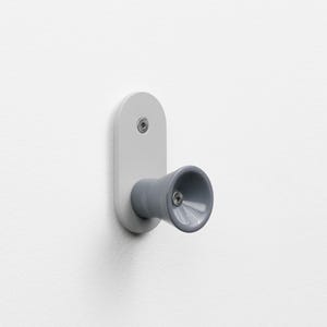 May include: A contemporary wall hook featuring a grey cylindrical body and a pale grey backplate. The hook is fixed to a white wall with screws. The design is minimalist and functional, suitable for various rooms. The hook's dimensions are approximately 10 cm in length.