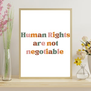 Może przedstawiać: Wydruk w ramie z tekstem "Prawa człowieka są niezbywalne" w kolorowych, pogrubionych literach. Tło jest białe, a rama złota.
