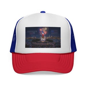 May include: A red, white, and blue trucker hat with a curved peak. The front panel displays a graphic of fireworks over the Statue of Liberty with the text "America's 250th". The hat has a white front, a red peak, and a blue mesh back.