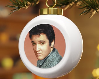 May include: White ceramic Christmas ornament with a photo of Elvis Presley in a round window. The photo shows Elvis looking to the left with a serious expression. The background of the photo is a light orange color.