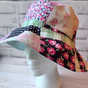 May include: A patchwork bucket hat with a floral and polka dot pattern. The hat features a variety of fabrics in pink, blue, green, and white. The brim is lined with a light blue fabric.