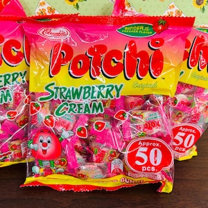 Może przedstawiać: Torby żelk&oacute;w truskawkowych "Porchi". Torby są r&oacute;żowe i ż&oacute;łte z czerwonym tekstem i postacią z kresk&oacute;wki truskawki. Każda torba zawiera około 50 cukierk&oacute;w.