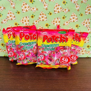 Może przedstawiać: Wyświetlanych jest kilka torebek cukierk&oacute;w "Porchi Strawberry Cream". Torebki są gł&oacute;wnie r&oacute;żowe i ż&oacute;łte, z nazwą produktu dużymi, kolorowymi literami. Każda torebka zawiera postać truskawki z kresk&oacute;wki i napis "Approx. 50 szt."