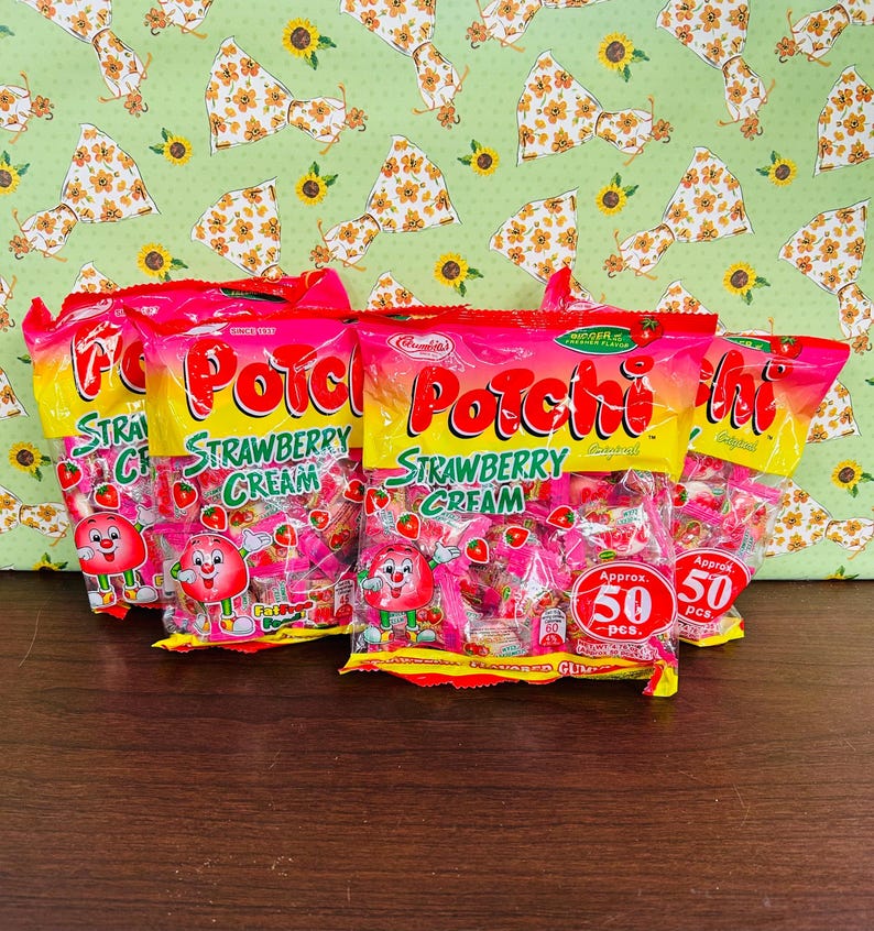 Może przedstawiać: Wyświetlanych jest kilka torebek cukierk&oacute;w "Porchi Strawberry Cream". Torebki są gł&oacute;wnie r&oacute;żowe i ż&oacute;łte, z nazwą produktu dużymi, kolorowymi literami. Każda torebka zawiera postać truskawki z kresk&oacute;wki i napis "Approx. 50 szt."