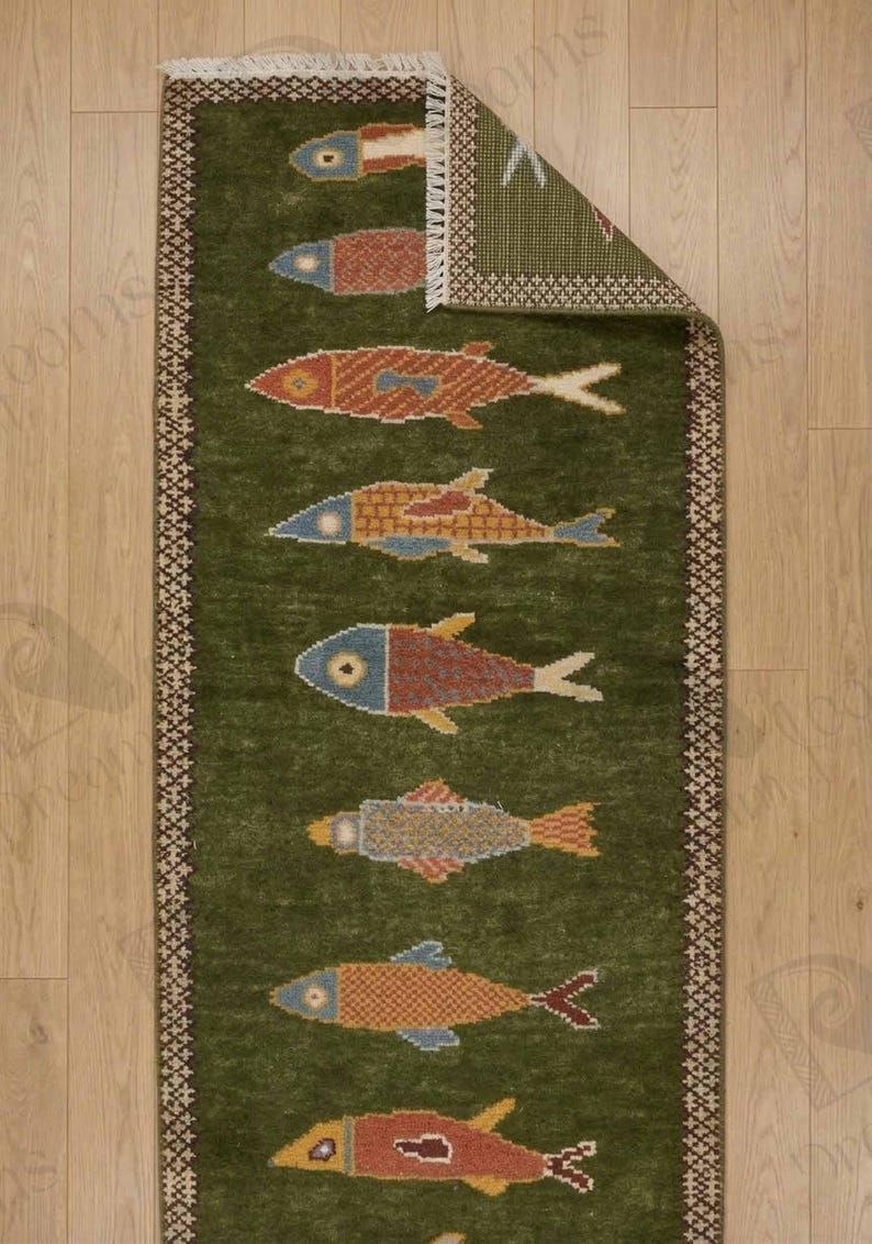 May include: A green rectangular rug with a repeating pattern of colorful fish. The fish are in shades of red, orange, blue, and yellow. The rug has a decorative border and fringe.