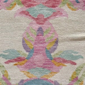 May include: A woven textile featuring a repeating symmetrical pattern in shades of pink, light blue, yellow, and green on an off-white background. The design consists of stylized floral and leaf motifs with a dense, textured, looped pile construction.