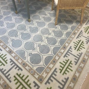 Könnte beinhalten: Ein hellblauer und weißer Teppich mit einem beige-grünen Rand. Der Teppich hat ein geometrisches Muster mit Kreisen und einem sich wiederholenden Muster.