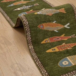 May include: A green runner rug with a repeating pattern of colorful fish. The fish are in shades of orange, yellow, blue, and red. The rug has a decorative border and is placed on a wooden floor.