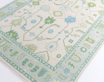 May include: A white rug with a blue and green geometric pattern. The rug has a fringe border.