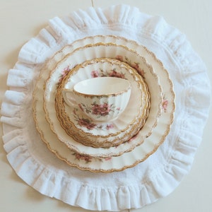 May include: A set of four white porcelain plates with gold trim and floral designs. The plates are stacked on top of each other and are sitting on a white doily.