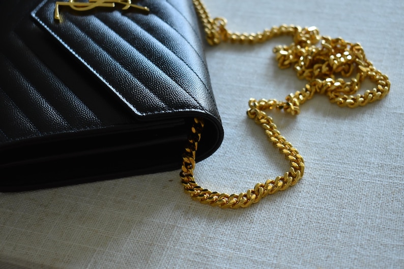 A black leather handbag with a gold chain strap is placed on a light-colored surface.