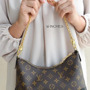 A person is holding a brown and gold Louis Vuitton handbag with a gold chain strap.