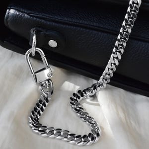 A close-up view of a black leather handbag with a gold chain strap and lock, resting on a white surface.