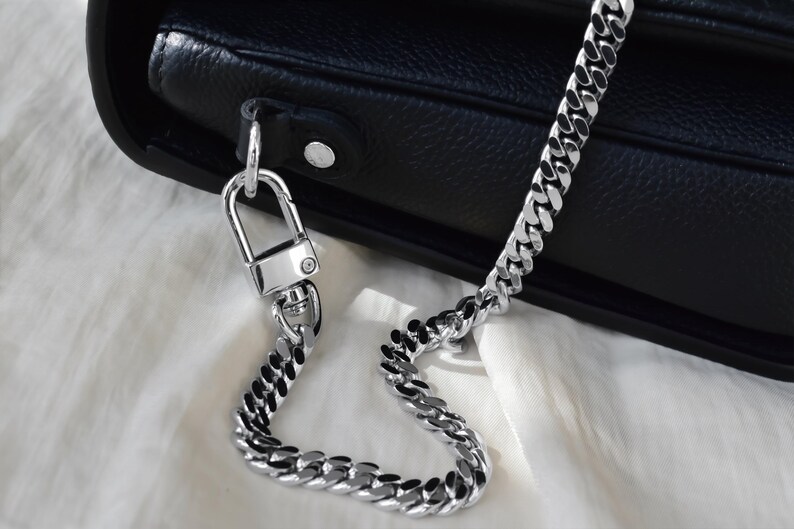 A close-up view of a black leather handbag with a gold chain strap and lock, resting on a white surface.