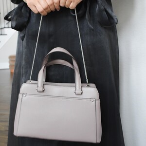 a woman in a black dress holding a gray purse