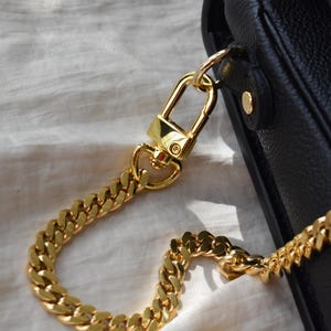 A close-up view of a gold chain strap and clasp on a black leather handbag.