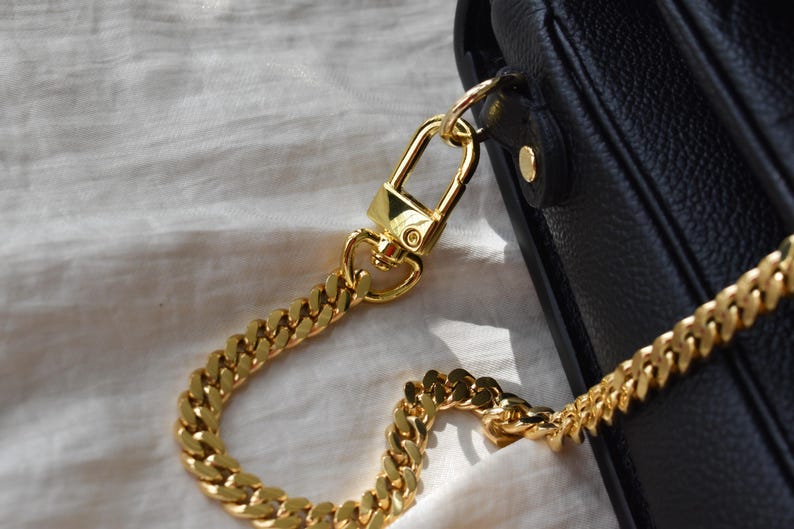 A close-up view of a gold chain strap and clasp on a black leather handbag.