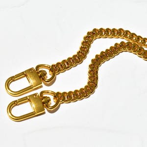 a pair of gold-colored metal chains with lock-like clasp-like ends, resting on a white background.