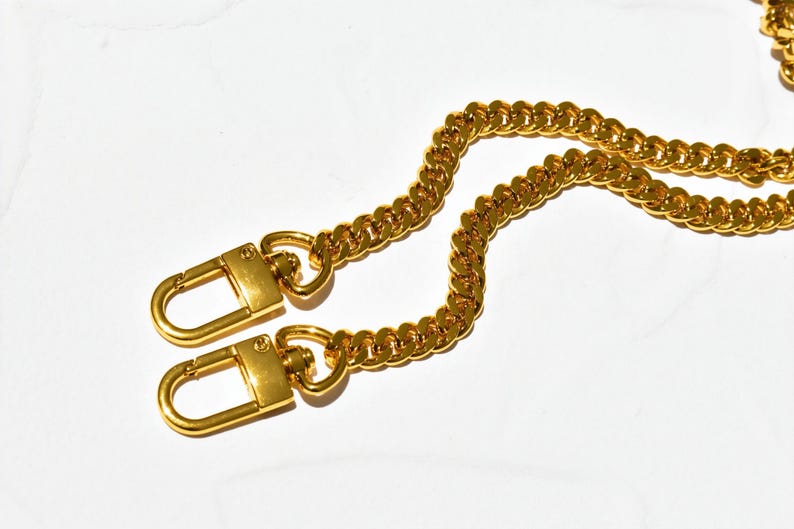 a pair of gold-colored metal chains with lock-like clasp-like ends, resting on a white background.