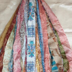 May include: A bundle of colorful fabric strips with various patterns, including floral, geometric, and paisley designs. The strips are tied together at the top and hang down in a cascade.
