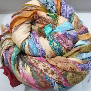 May include: A colorful bundle of silk ribbon scraps in shades of pink, blue, green, orange, and brown. The ribbon is woven together in a spiral pattern, creating a unique and textured look.