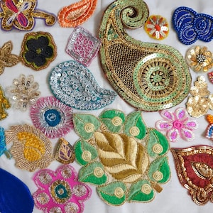 May include: A collection of assorted embroidered and sequined fabric patches in various shapes and colors, including paisley, floral, and geometric designs featuring gold, silver, green, pink, blue, and red thread and metallic embellishments.