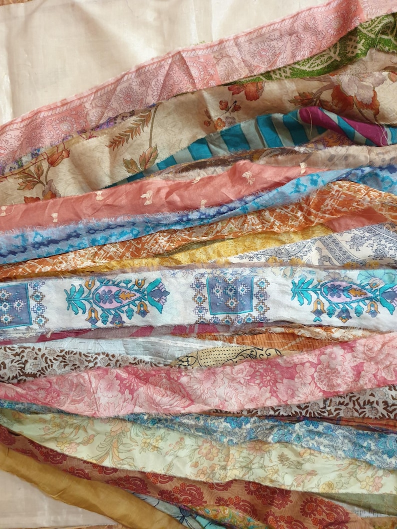 May include: A collection of colorful silk fabric scraps in various patterns and textures. The fabric scraps are arranged in a layered, cascading design, creating a visually appealing and textured display.
