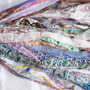 May include: A collection of colorful fabric strips, featuring a variety of patterns and textures. The strips are in shades of blue, purple, green, and cream, with floral and geometric designs. The fabric appears to be silk or a similar lightweight material.