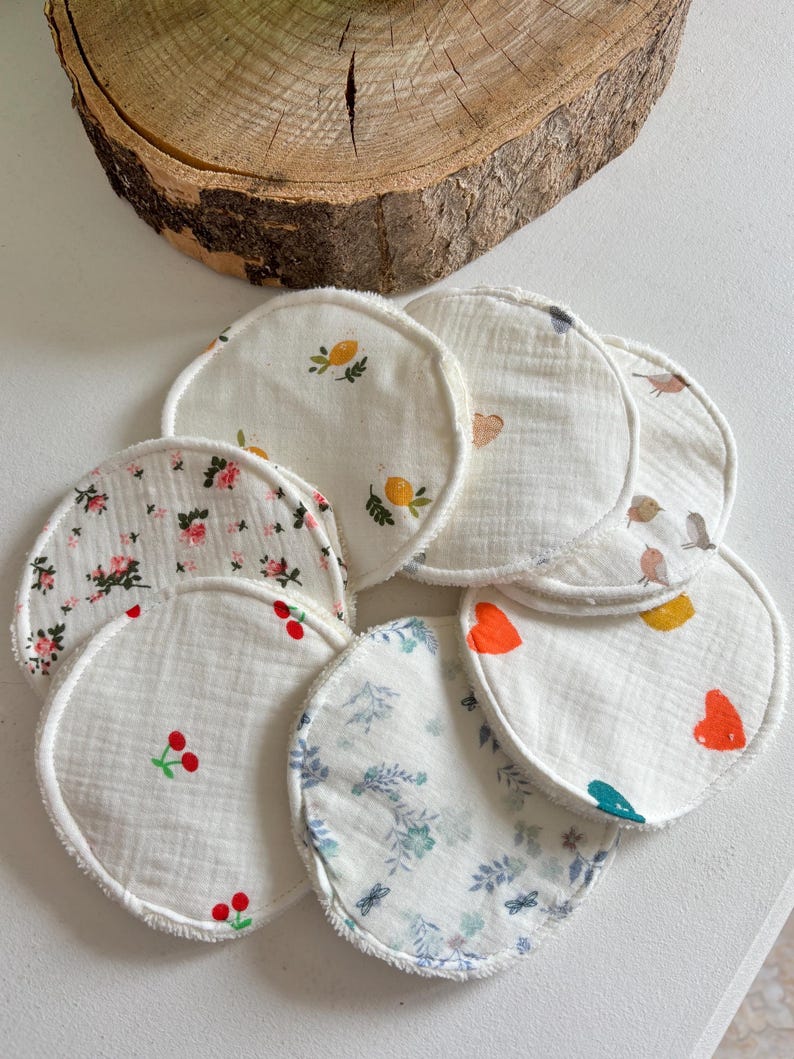 May include: A selection of round, white fabric pads with diverse printed designs. Some pads feature floral patterns, cherries, lemons, birds, and hearts. The pads have a white, textured border and are arranged on a white surface.