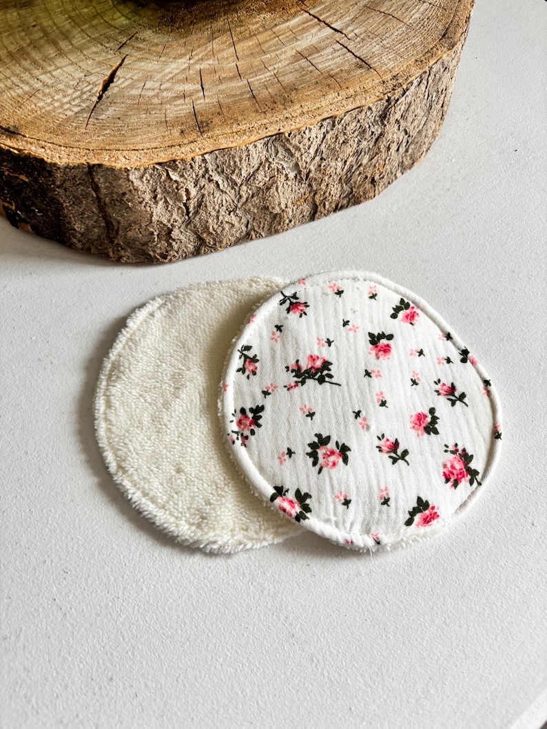 May include: Two reusable facial rounds. One is white terry cloth, the other is white with a pink floral pattern. The rounds are circular and sit on a white surface, with a wooden slice in the background.