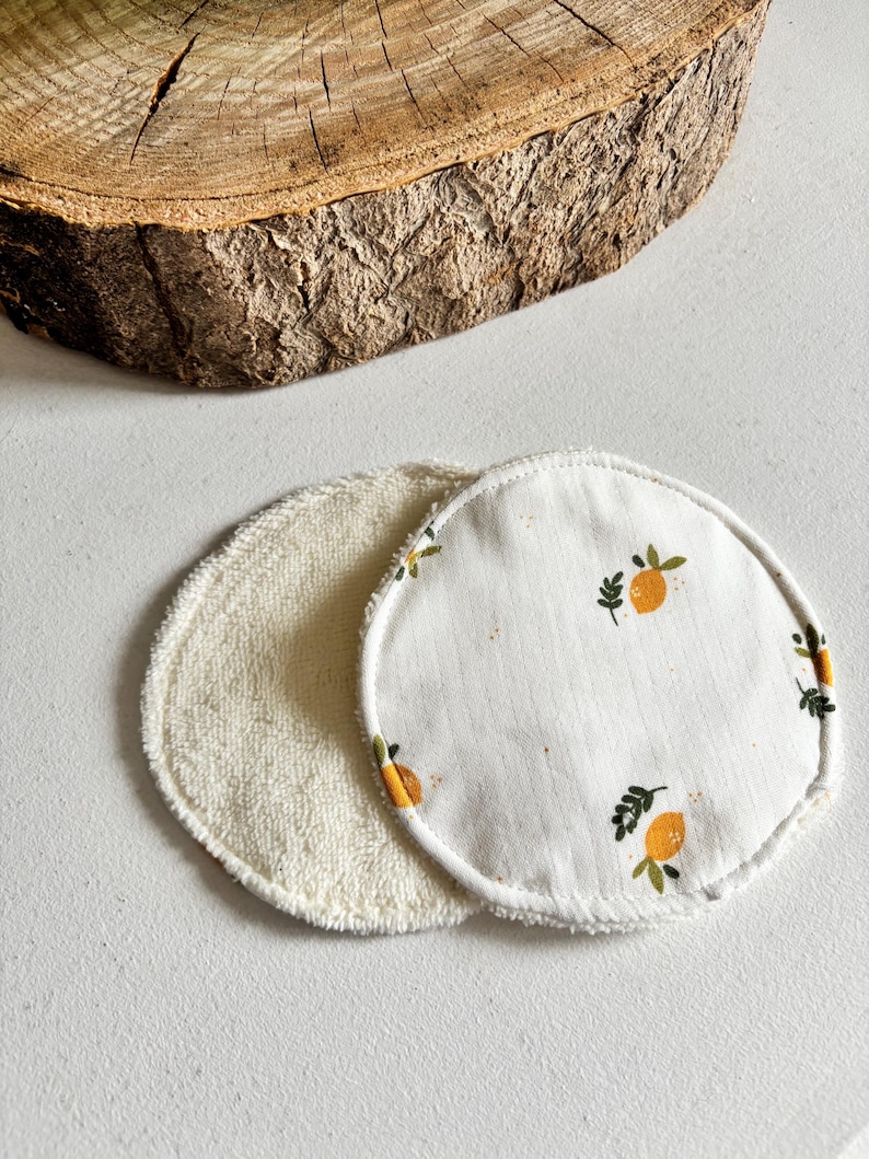 May include: Two reusable facial rounds. One is a soft, cream-coloured terry cloth. The other is white with a pattern of orange lemons and green leaves. The rounds are circular and have a stitched edge.
