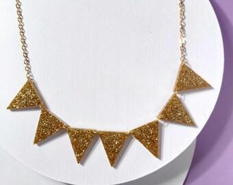 May include: A gold necklace with a series of glittery triangle pendants. The pendants are arranged in a banner-like design, suspended from a delicate gold chain. The necklace is displayed against a white background.