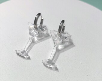 May include: A pair of hoop earrings featuring clear, transparent martini glass charms. The earrings are constructed with silver-toned metal hoops attached to the top of each miniature glass-shaped pendant, creating a cohesive set of jewellery.